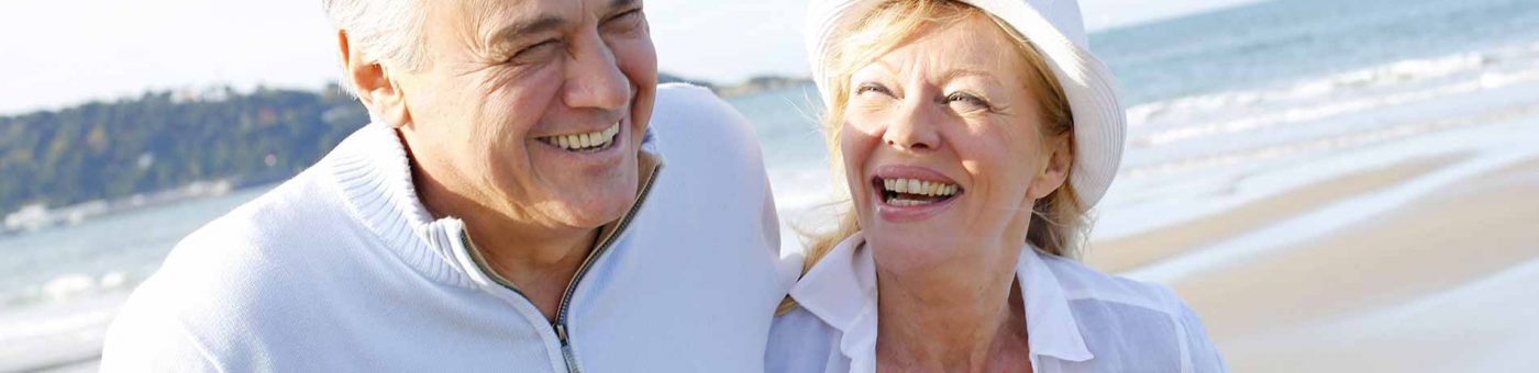 older couple walking on the beach laughing after having cataract surgery